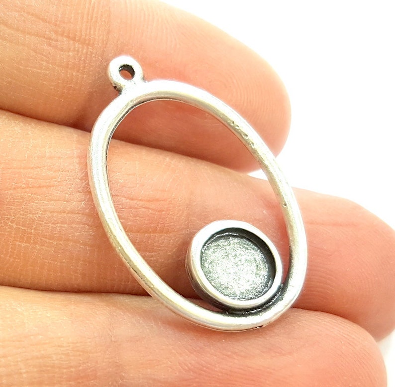 May include: Silver oval pendant with a smaller circle cutout in the center. The pendant has a loop at the top for attaching a chain.