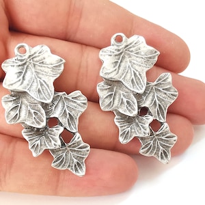 May include: Two silver-toned metal charms shaped like clusters of ivy leaves. Each charm has three leaves with detailed textured surfaces.