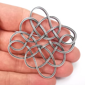 May include: A silver-colored Celtic knot brooch with an intricate interwoven design. The brooch features a complex pattern of loops and curves, creating a symmetrical and ornamental piece. The metal has a slightly aged appearance, enhancing the detail of the design.