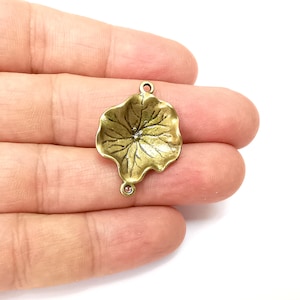 May include: Gold-toned metal charm shaped like a leaf with a detailed design. The charm has two jump rings for attaching to jewelry or other crafts.