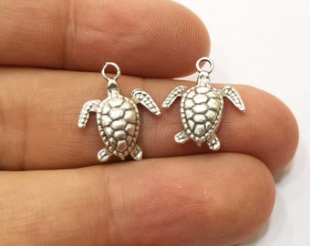 May include: Two silver turtle charms with a detailed shell design. The charms have a loop at the top for attaching to jewelry.