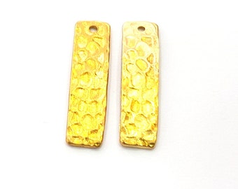 Può includere: Due ciondoli a barra in metallo color oro con una texture martellata. Ogni ciondolo ha un piccolo foro nella parte superiore per attaccare una catena o un cordino.