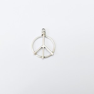 May include: Silver peace sign charm pendant. The charm is a simple, circular design with a peace sign in the center.