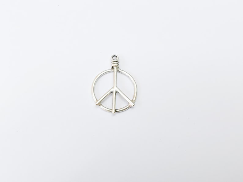 May include: Silver peace sign charm pendant. The charm is a simple, circular design with a peace sign in the center.