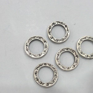 May include: Five silver-toned metal rings with an ornate design. The rings are all the same size and shape.