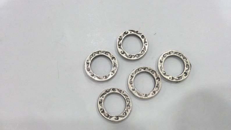 May include: Five silver-toned metal rings with an ornate design. The rings are all the same size and shape.