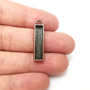 May include: A rectangular metal pendant with a black interior and a bronze finish. The pendant has a loop at the top for attaching a chain or cord.
