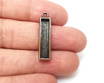 May include: A rectangular metal pendant with a black interior and a bronze finish. The pendant has a loop at the top for attaching a chain or cord.