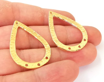 Può includere: Due pendenti in metallo dorato a forma di lacrima con una texture martellata. Ogni pendente ha quattro fori attorno al bordo.