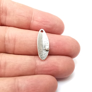 May include: Silver oval pendant with a textured surface and a small bead accent.