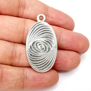 Puede incluir: Pendiente ovalado de plata con un diseño de círculo concéntrico en espiral.