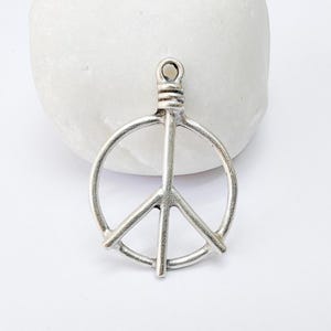 May include: Silver peace sign charm pendant. The charm is a simple, open circle with a peace sign inside. The charm has a loop at the top for attaching to a necklace or bracelet.