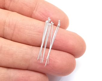 May include: A close-up of a hand holding a bundle of silver head pins with round heads. The pins are approximately 1 inch long.