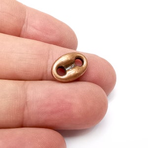 Op de afbeelding: Een ovale toggle-sluiting in koperkleur met twee gaten. De sluiting is ontworpen voor gebruik in sieraden maken of andere knutselprojecten.