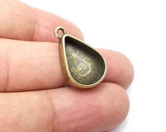 Puede incluir: Un colgante de color bronce con una bisel en forma de lágrima para engastar una piedra o resina. El colgante tiene un bucle en la parte superior para sujetar una cadena o cordón.
