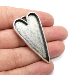 May include: A silver heart-shaped pendant with a smooth, slightly textured surface. The pendant has a loop at the top for attaching a chain.