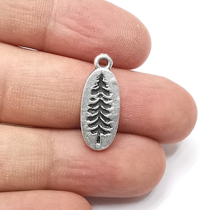 May include: Silver charm with a detailed pine tree design. The charm is oval shaped and has a loop at the top for attaching to a necklace or bracelet.