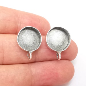 May include: Two silver-toned round pendant trays with a loop at the bottom. The trays are designed to hold a round cabochon.