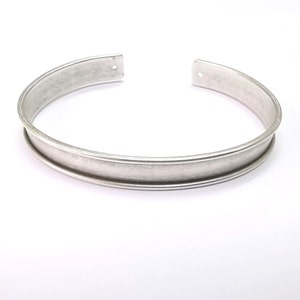 Puede incluir: Un brazalete de plata con un acabado liso y ligeramente texturizado.