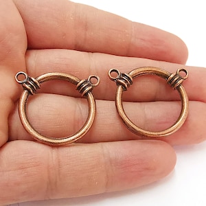 May include: Two copper-toned metal rings with a decorative twisted design. Each ring has two small loops for attaching to other jewellery pieces.