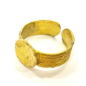 May include: A gold-coloured ring with a textured band and a round, flat top. The ring is made of metal and has a simple design.
