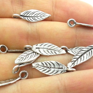 May include: Silver tone leaf shaped charms with a loop at the top. The charms are about 1 inch long and have a detailed leaf design.