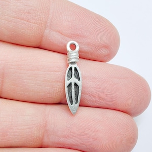 Peut inclure: Un petit charme argenté en forme de flèche ou de feuille stylisée. Le charme a une boucle en haut pour l'attacher à une chaîne ou à d'autres bijoux. Le design comprend une ligne verticale centrale avec trois lignes horizontales, créant un motif unique.