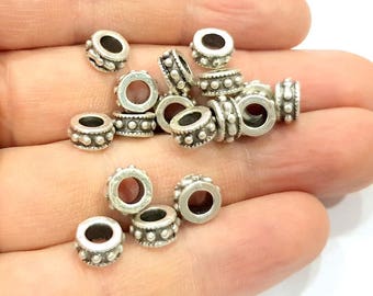 May include: A collection of silver-toned metal spacer beads with a textured design. The beads are round with a hole in the center and have a raised pattern of small dots.