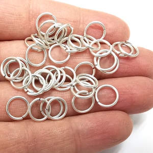May include: A pile of silver jump rings, a type of jewellery finding, in a hand. The rings are small and round, and they are perfect for making jewellery.