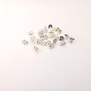 May include: A pile of silver earring backs, also known as earring stoppers, on a white background.
