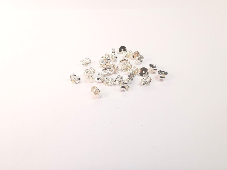 May include: A pile of silver earring backs, also known as earring stoppers, on a white background.
