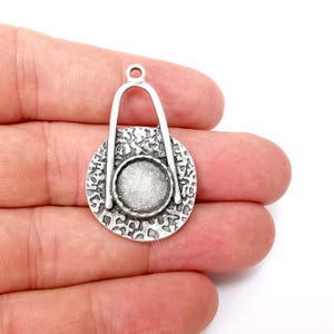 Op de afbeelding: Zilveren hanger met een getextureerde ronde schijf en een lus aan de bovenkant. De schijf heeft een kleinere ronde opening in het midden.