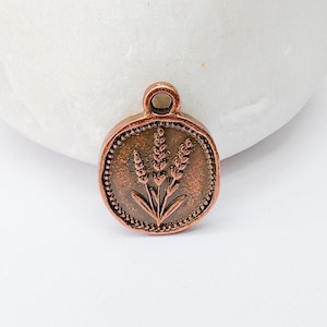 May include: A round, copper-colored pendant with a wheat stalk design. The pendant has a small loop at the top for hanging and a beaded border. The wheat design is in the center of the pendant.