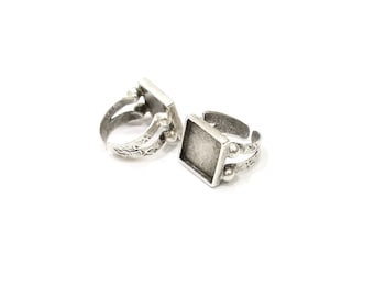 May include: Two silver adjustable rings with square bezels for setting cabochons. The rings have a textured finish and are designed to hold a 12mm square cabochon.