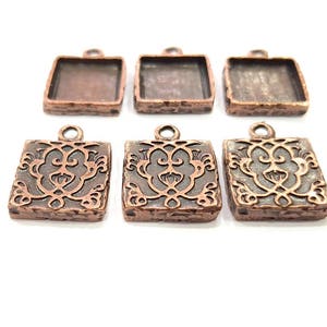 Puede incluir: Seis colgantes de metal de color cobre con forma cuadrada. Tres colgantes tienen una superficie lisa y tres colgantes tienen un diseño intrincado en relieve.