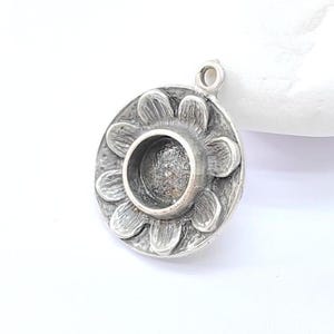 Op de afbeelding: Zilveren hanger met een bloemmotief en een ronde bezel voor een cabochonsteen.