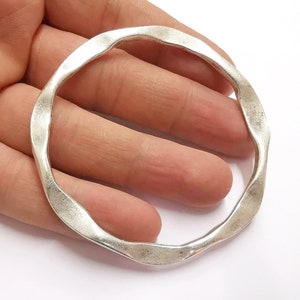 May include: A silver-toned, open-ended bangle bracelet with a wavy, textured design.