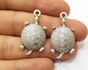 May include: Two silver turtle charms with a detailed shell design. The charms have a loop at the top for attaching to jewelry or other crafts.