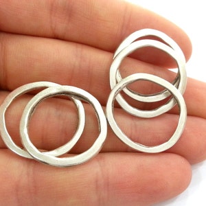 May include: Four silver metal rings, each with a slightly different size and shape, are stacked on top of each other. The rings are smooth and have a polished finish.