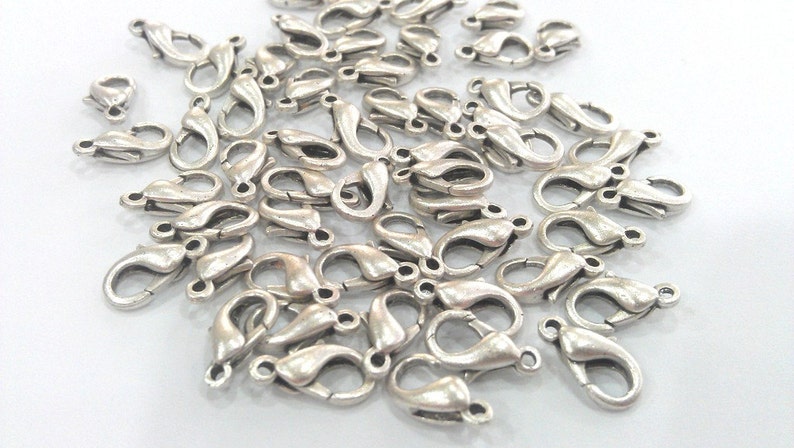 May include: A pile of silver-toned metal lobster claw clasps, commonly used for jewelry making.