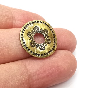 以下が含まれることがあります： 中央に穴が開いた幾何学模様の円形デザインが施された金色調の金属製チャーム