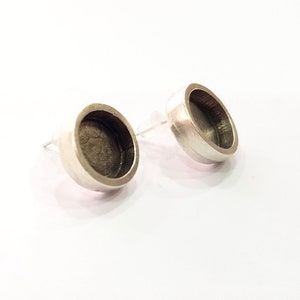 May include: A pair of silver stud earrings with a round, slightly concave design. The earrings have a simple, minimalist style.