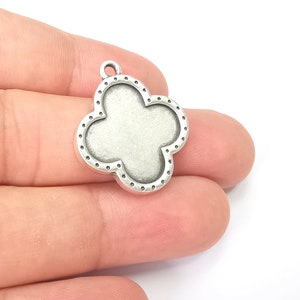 May include: Silver-toned metal charm shaped like a four-leaf clover with a dotted border.