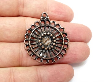May include: A copper-colored metal pendant with a circular design featuring a central sunburst pattern surrounded by a decorative border.