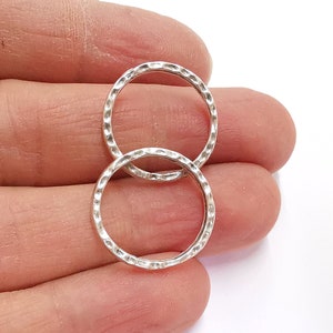 May include: Two silver rings with a textured finish. The rings are interlocked and are shown on a hand.