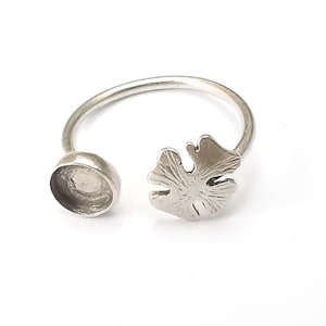 May include: Silver ring with a round bezel setting and a leaf design. The ring is open on one side.