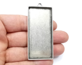 May include: Silver pendant tray with a rectangular shape and a smooth, shiny surface. The tray is designed to hold a small piece of art or jewellery.