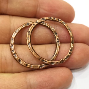 May include: Two hammered copper rings, each with a textured surface, are shown together. The rings are a warm, metallic copper color.