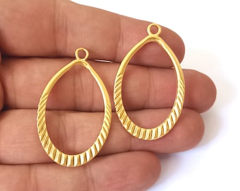 May include: Two gold-colored metal oval-shaped pendant blanks with a textured design. The blanks have a small loop at the top for attaching a chain or cord.