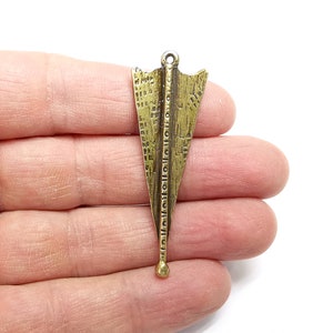 May include: A gold-toned metal arrowhead pendant with a detailed geometric design. The pendant has a loop at the top for attaching to a chain or cord.